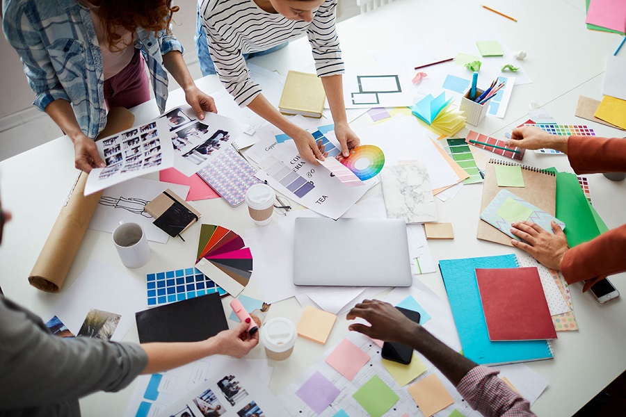 The Role of Creativity in Developing Successful Business Strategies Top-down view of a design team around a table with color swatches, photos, and sketches.